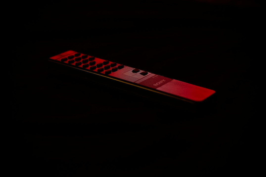 Hand holding an old television remote control in front of a glowing screen